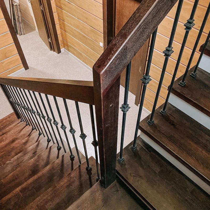 Г-образная деревянная лестница из ясеня с ковкой в брусовом доме